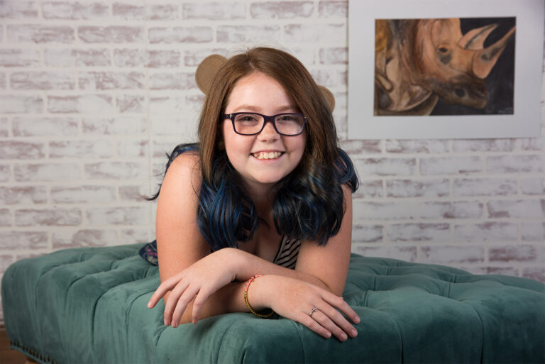 Preteen girl with brown and blue hair and freckles and glasses laying on green ottoman in Winter Garden, Florida