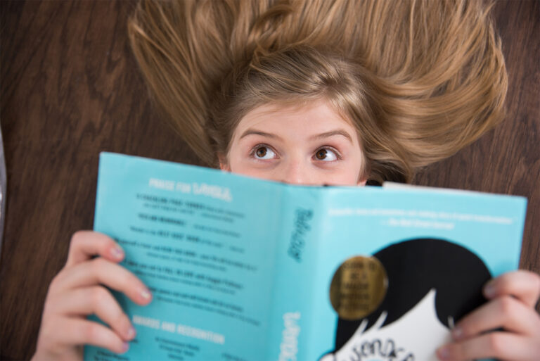 Blonde preteen girl with brown eyes laying on floor reading a book in Winter Garden, Florida