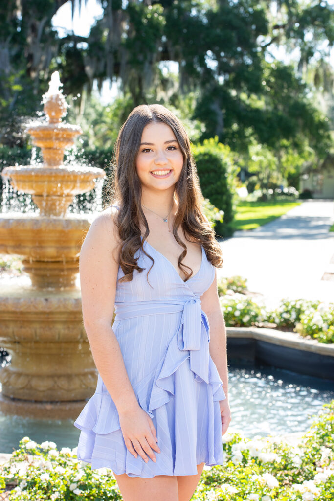 High school senior brunette girl in blue dress in front of fountain and roses