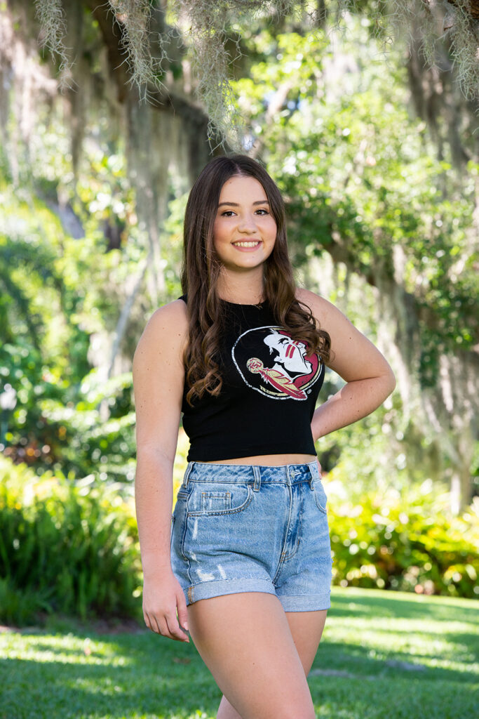 High school senior brunette girl in UF clothing under oak trees