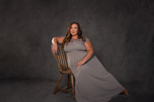 Fine art portrait of curvy woman sitting in chair on grey background