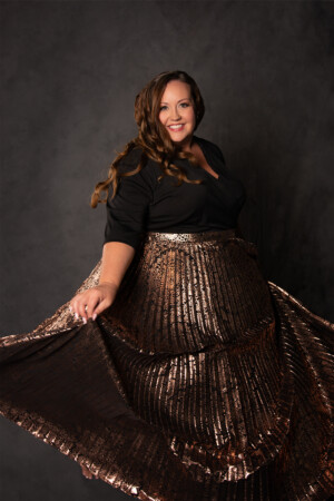 Fine art portrait of curvy woman in black and copper dress spinning in front of grey background
