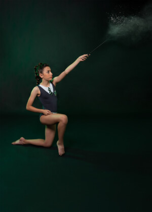 Photo of preteen 11 year old gymnast with wand and magic in Slytherin leotard on green background in studio in Ocoee Florida. Gymnast photography